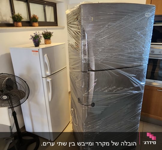 מקרר עטוף בניילון לצד מקרר נוסף ומאוורר בחדר